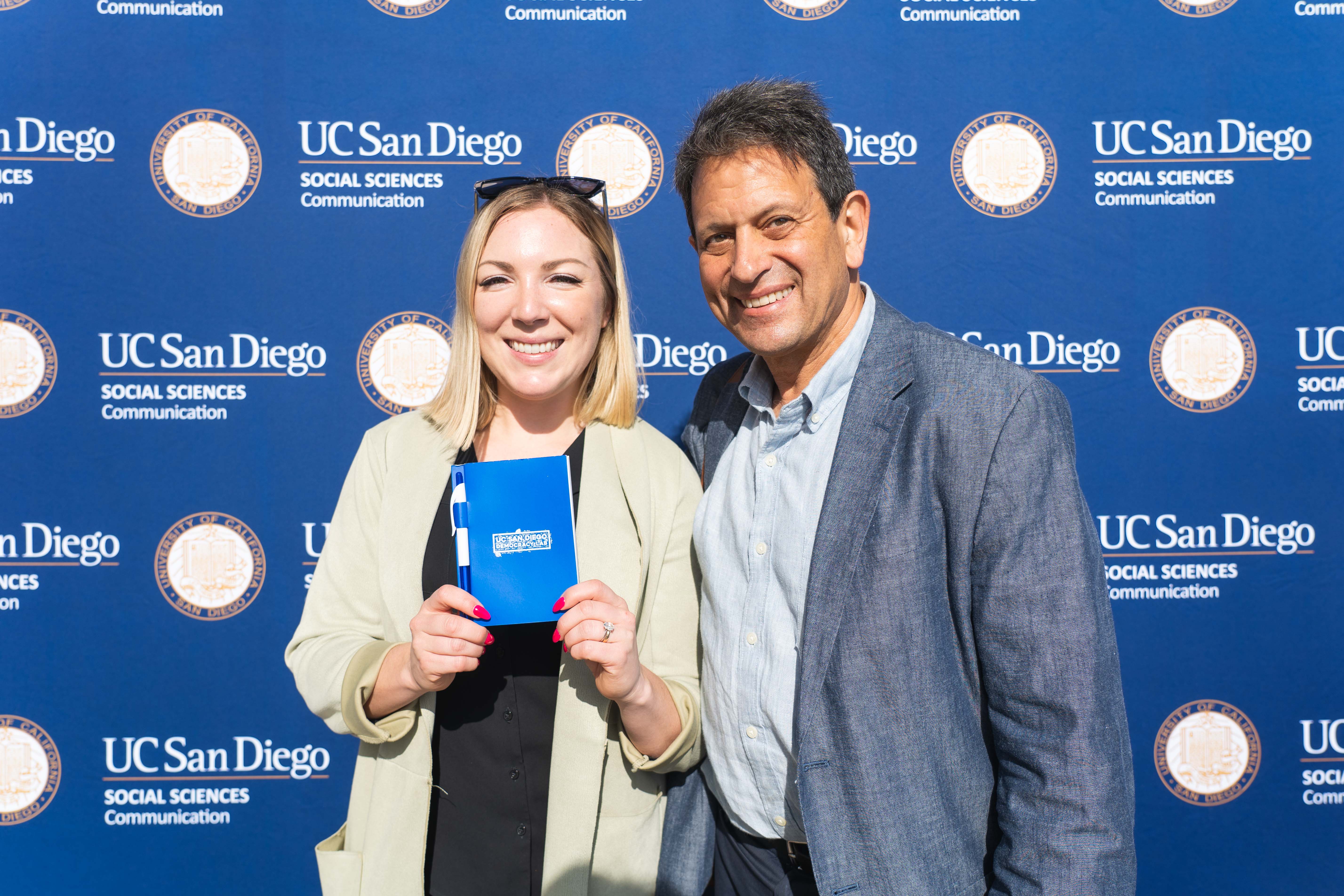 Department Chair Brian Goldfarb and MSO Taylor Benrieh hold Democracy Lab swag in front of a step and repeat banner with UCSD Department of Communication logos