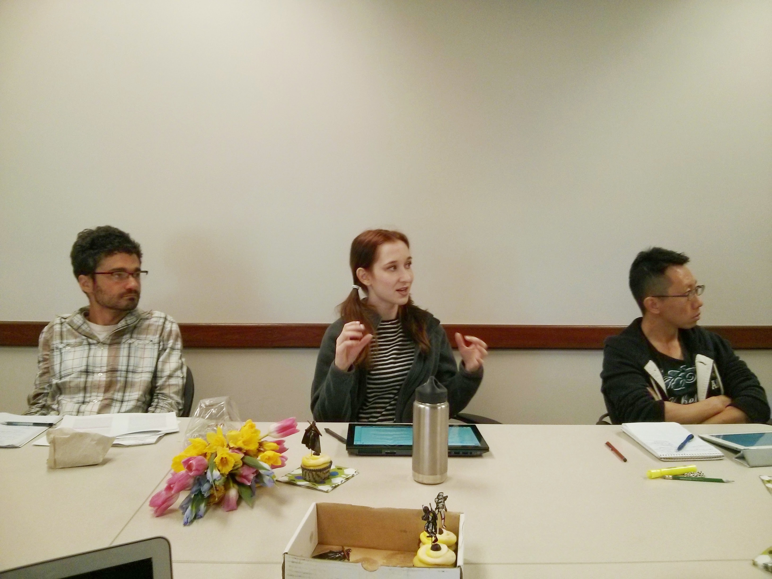 three graduate students sit around a white table gesticulating to a discussion on Situated Practices