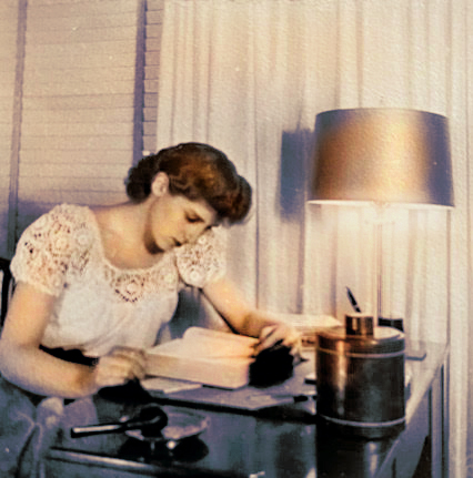 A young Anita Schiller works by lamplight over a book at her desk