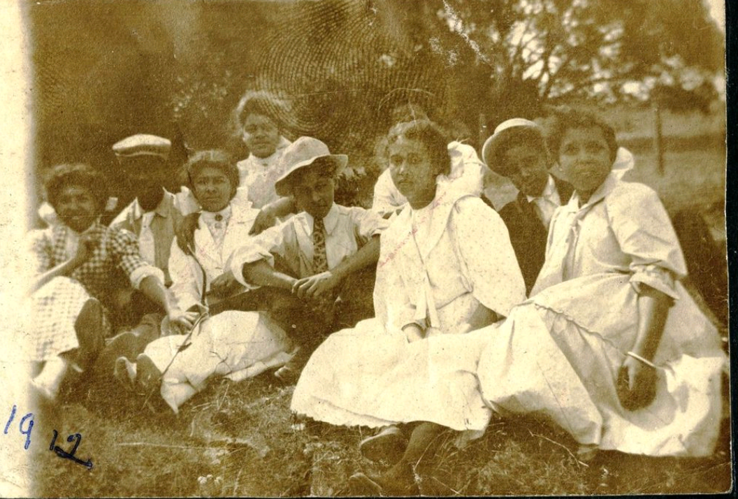 sepia toned antique photo of a dozen Black people in early 1900s clothing sitting